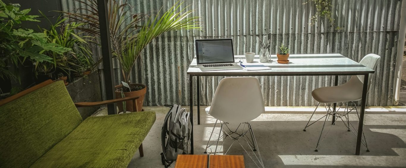 Ein moderner Arbeitsplatz mit Tisch, Laptop und Pflanzen in einem hellen, minimalistischen Raum.